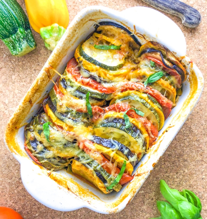 A small oven dish with colorful baked vegetable slices, topped with cheese