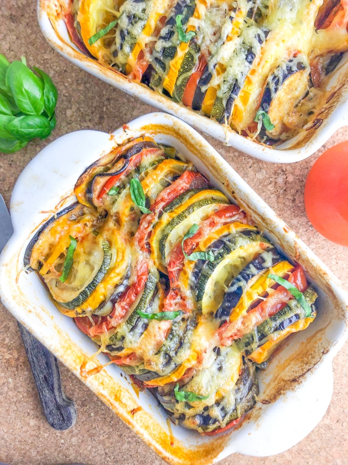 Two oven dishes with colorful baked vegetable slices, topped with grated cheese