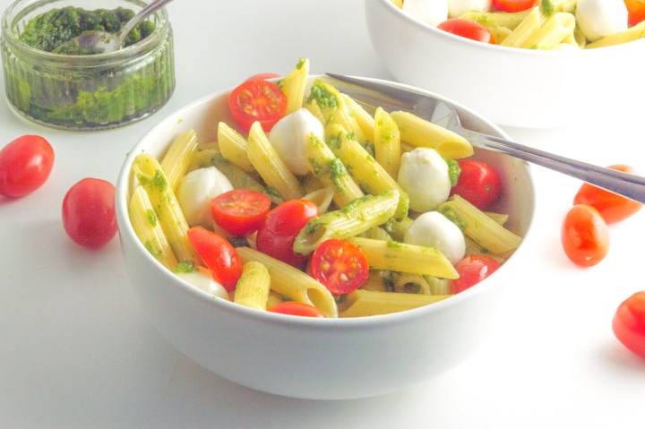 taça com salada de massa caprese com pesto num recipiente e tomates espalhados