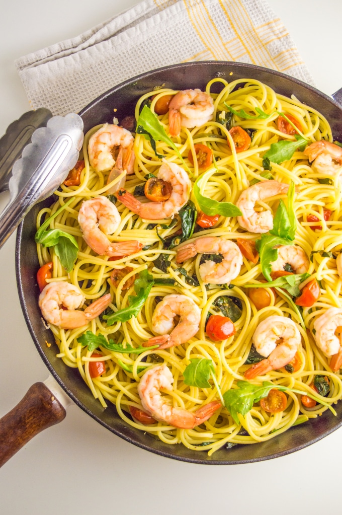 A skillet with shrimp, tomatoes and spinach pasta topped with arugula