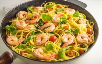 close-up of a skillet with shrimp, tomatoes and spinach pasta topped with arugula