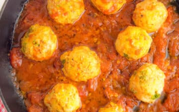 A cast iron skillet on a table filled with nine turkey meatballs cooked in tomato sauce