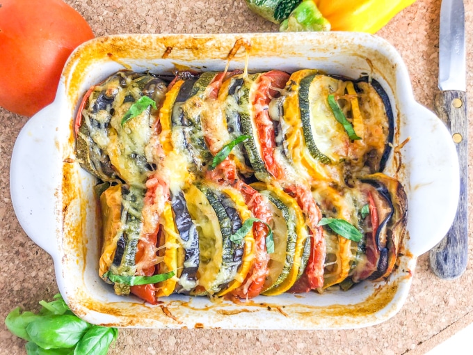 Close-up of an oven dish with colorful baked vegetable slices, topped with cheese