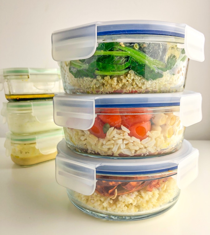 three filled lunchboxes and three dressing containers, both stacked