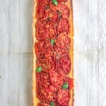Uma tarte rectangular, recheada de tomates e guarnecida com folhas de manjericão