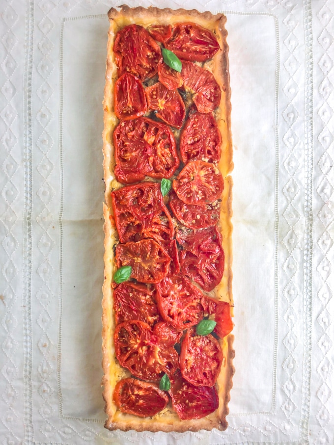 A rectangular shaped tart filled with tomatoes and garnished with basil leaves