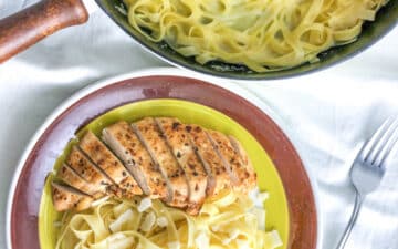 A plate with fettuccine alfredo with chicken and a skilled with pasta
