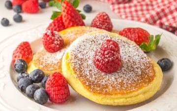 closeup of a plate with a fluffy pancake topped with raspberries