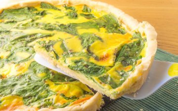 lifting a slice of spinach and cheese quiche after cuttingt