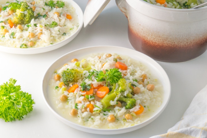 dois pratos com arroz de legumes e panela de barro ao fundo