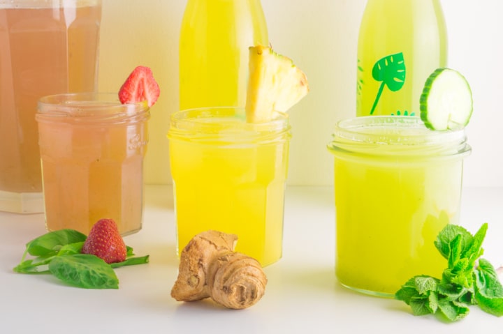 três copos com refrescos de cor rosa, amarela e verde e decorados com frutas e folhas